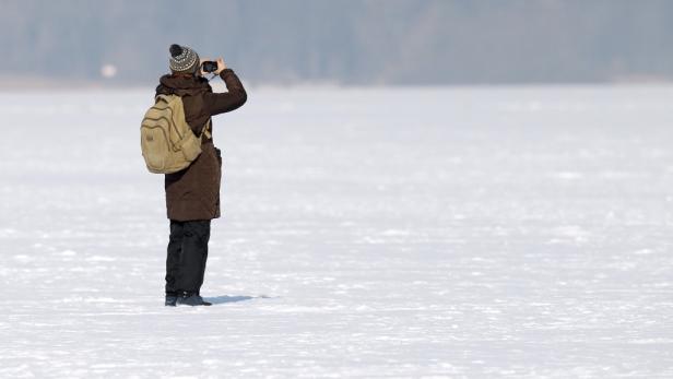 Eine Person mit Rucksack fotografiert eine verschneite Landschaft.