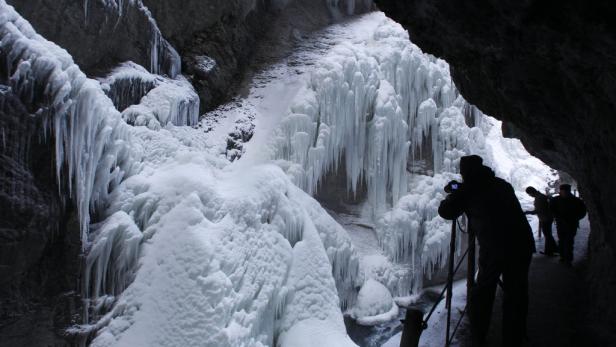 Menschen besuchen eine Eishöhle mit großen Eiszapfen.