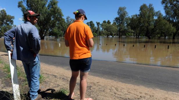 Zwei Personen stehen an einer überfluteten Straße und betrachten das Hochwasser.