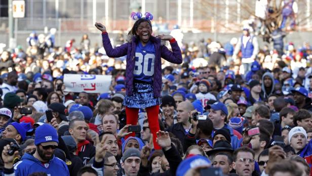 Eine junge Frau im Giants-Trikot steht auf einer Menschenmenge und jubelt.