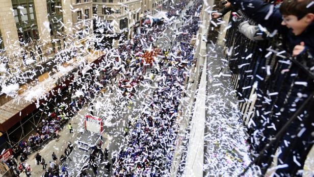 Konfetti fällt auf eine Menschenmenge während einer Parade in einer Stadt.