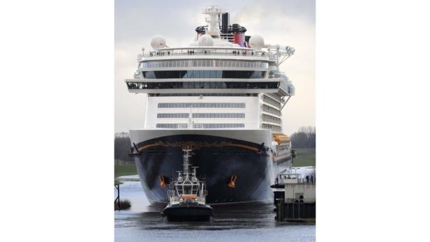 Ein Schlepper zieht ein großes Kreuzfahrtschiff durch einen Kanal.