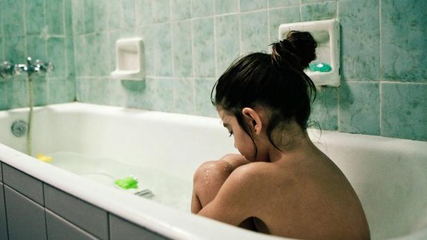 Ein Mädchen sitzt in einer Badewanne mit Spielzeug und umarmt ihre Knie.