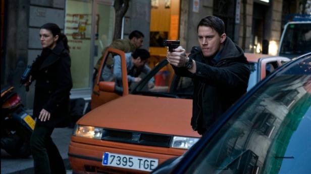 Gina Carano und Channing Tatum zielen mit Waffen in einem belebten Stadtgebiet.