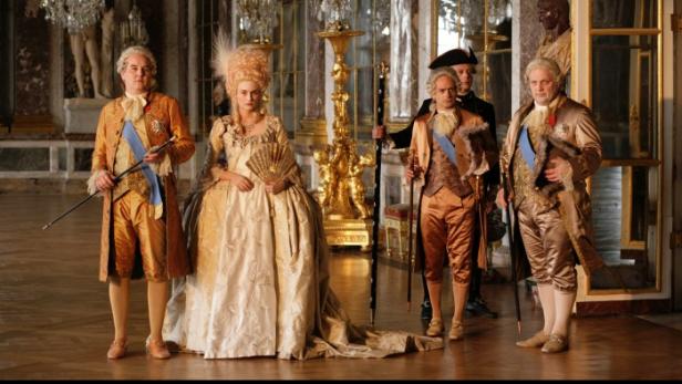 Szene mit Personen in Kostümen des 18. Jahrhunderts in einem opulenten Ballsaal.