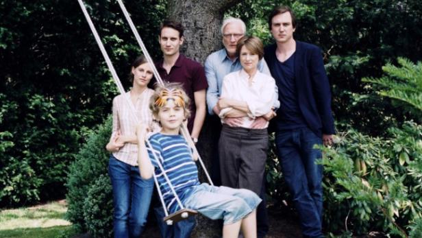 Eine Familie posiert vor einem Baum, ein Kind sitzt auf einer Schaukel.