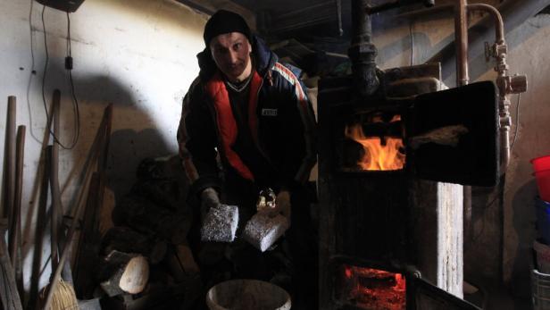 Ein Mann mit Mütze steht vor einem Ofen mit brennendem Feuer.