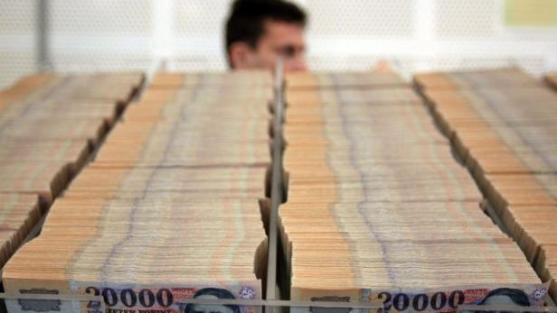 Ein Mann steht hinter mehreren Bündeln von 20.000 Forint Banknoten.