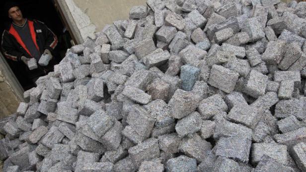Ein Mann hält einen Block aus recyceltem Material vor einem großen Haufen weiterer Blöcke.