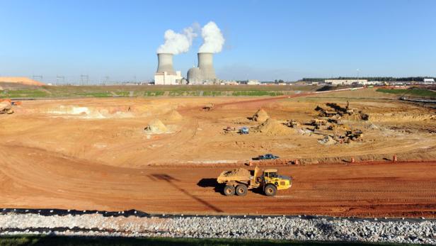 Ein gelber Muldenkipper auf einer Baustelle mit einem Kernkraftwerk im Hintergrund.