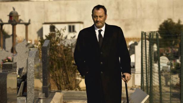 Jean Reno geht mit einem Stock über einen Friedhof.