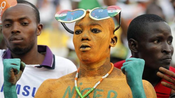 Ein Fan mit Körperbemalung in den Farben des Niger jubelt mit erhobener Faust.