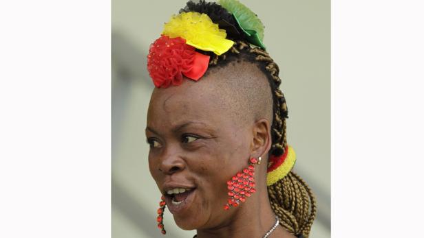 Eine Frau mit einem bunten Haarschmuck und roten Ohrringen blickt zur Seite.