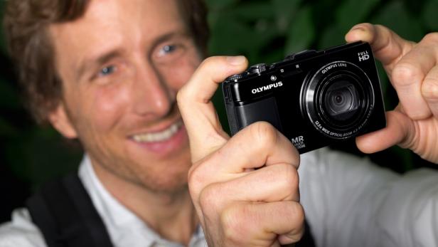 Ein Mann hält eine schwarze Olympus-Kamera in seinen Händen.