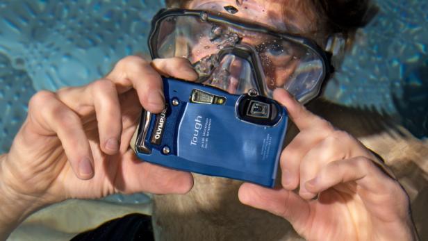 Ein Mann mit Taucherbrille fotografiert unter Wasser mit einer blauen Olympus Tough Kamera.
