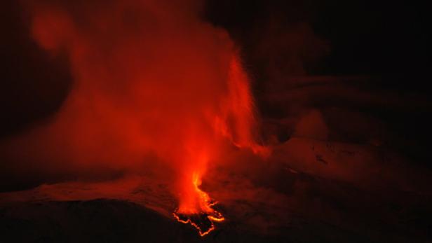 Ein Vulkan bricht aus und speit Lava und Rauch in den dunklen Nachthimmel.