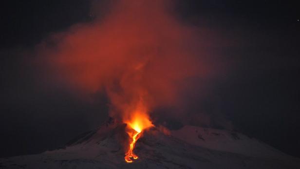Ein Vulkan bricht nachts aus und speit Lava und Rauch aus.