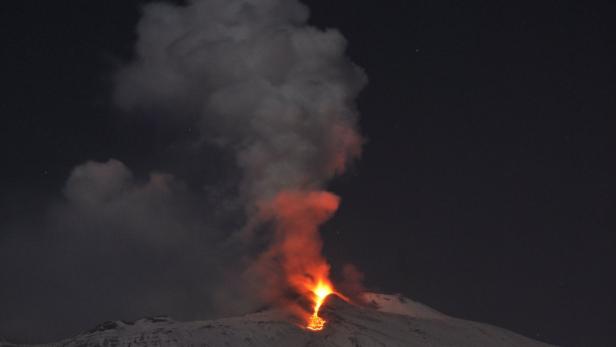 Ein schneebedeckter Vulkan bricht nachts aus und speit Lava und Rauch aus.