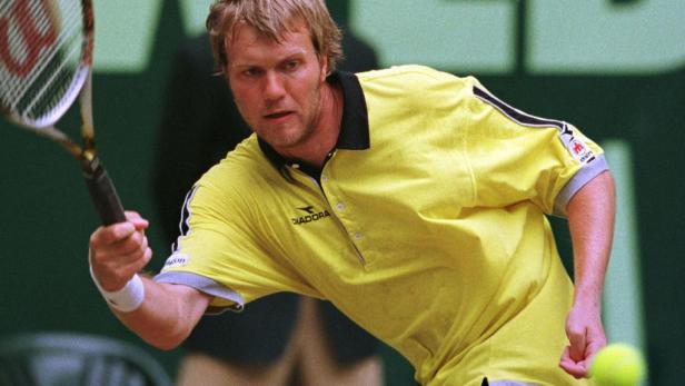 Ein Tennisspieler in einem gelben Hemd schlägt einen Ball.