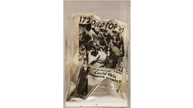 Eine zerknitterte Zeitung in einer transparenten Vitrine.