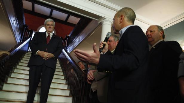 Newt Gingrich steht auf einer Treppe, während eine Person ins Mikrofon spricht.