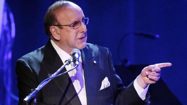 Clive Davis spricht bei einer Veranstaltung und zeigt mit dem Finger.