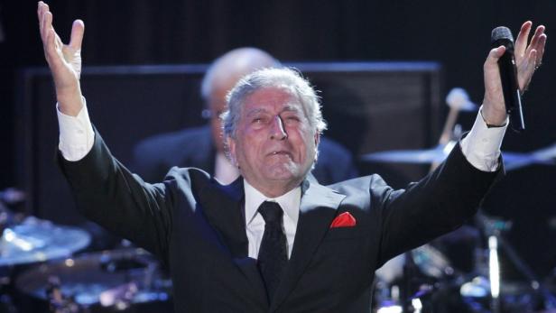 Tony Bennett steht mit erhobenen Armen und einem Mikrofon auf der Bühne.