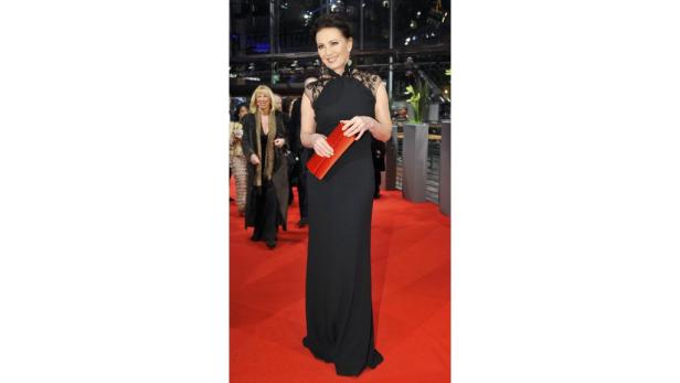 Eine Frau in einem schwarzen Abendkleid mit roter Clutch auf einem roten Teppich.