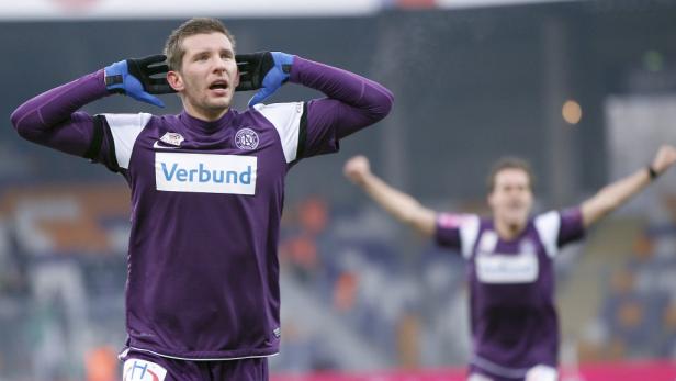 Ein Fußballspieler jubelt mit erhobenen Händen auf dem Spielfeld.