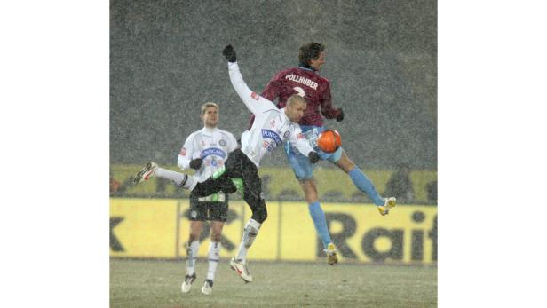 Zwei Fußballspieler kämpfen im Schneefall um den Ball, ein weiterer Spieler steht im Hintergrund.
