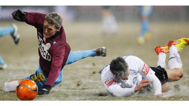 Zwei Fußballspieler kämpfen bei regnerischem Wetter um den Ball.