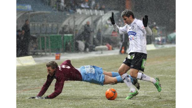 Bei Schneefall kämpfen zwei Fußballspieler um den Ball.