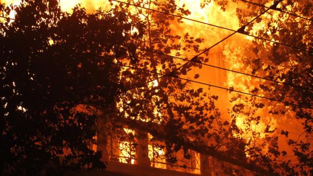 Ein Gebäude steht in Flammen, teilweise verdeckt durch Bäume und Stromleitungen.