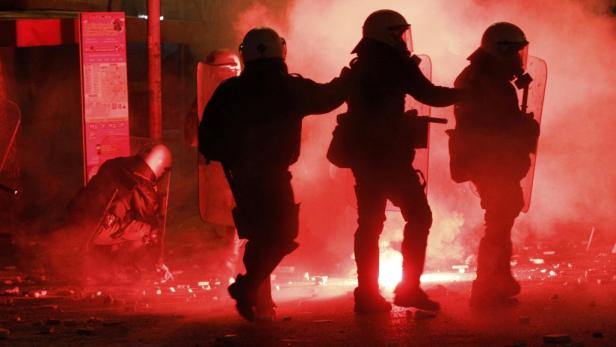 Polizisten in Schutzausrüstung stehen inmitten von rotem Rauch.