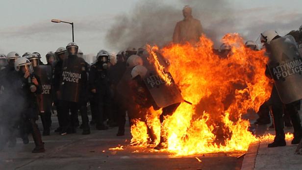 Eine Gruppe Polizisten in Schutzausrüstung steht vor einem großen Feuer.