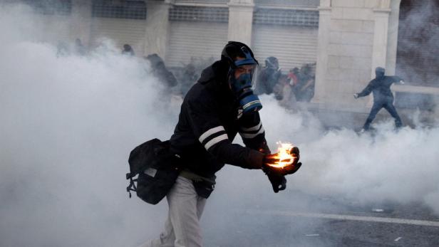 Eine Person mit Gasmaske hält einen brennenden Gegenstand inmitten von Rauch.
