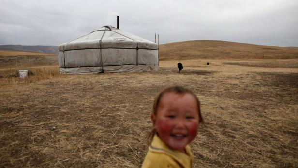 Ein lächelndes Kind steht vor einer traditionellen mongolischen Jurte in einer weiten Landschaft.