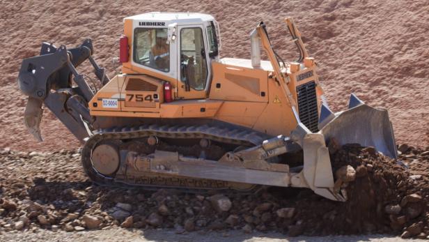 Ein orangefarbener Liebherr-Bulldozer schiebt Erde vor einem Erdhügel zusammen.