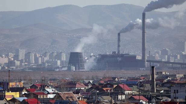 Rauch steigt aus den Schornsteinen einer Fabrik in einer Stadtlandschaft.