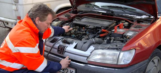 Ein Mann in einer Warnjacke repariert den Motor eines roten Peugeot.
