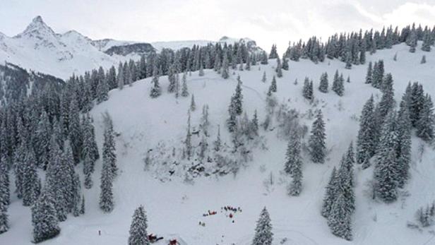 Eine verschneite Berglandschaft mit Tannenbäumen und einer Gruppe von Menschen im Tal.