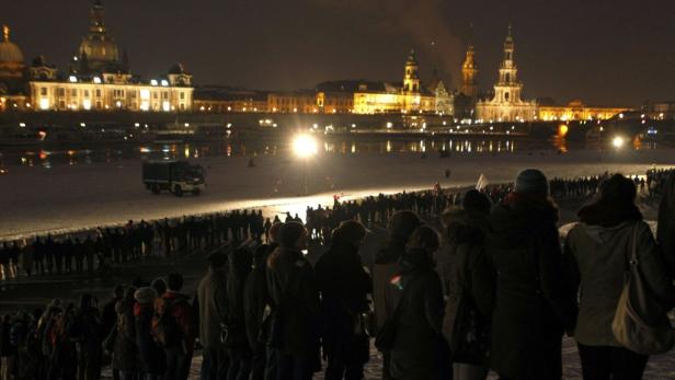 Eine Menschenmenge versammelt sich nachts in Dresden vor der beleuchteten Altstadt.
