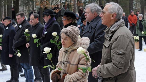 Eine Gruppe von Menschen hält weiße Rosen bei einer Trauerfeier im Freien.
