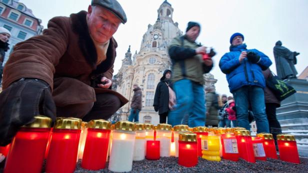 Menschen zünden Kerzen vor der Frauenkirche in Dresden an.