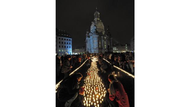 Menschen zünden Kerzen vor der Frauenkirche in Dresden an.