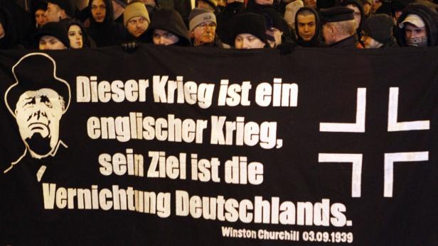 Demonstranten halten ein Banner mit einem Zitat von Winston Churchill und einer stilisierten Eisernen Kreuz-Darstellung.