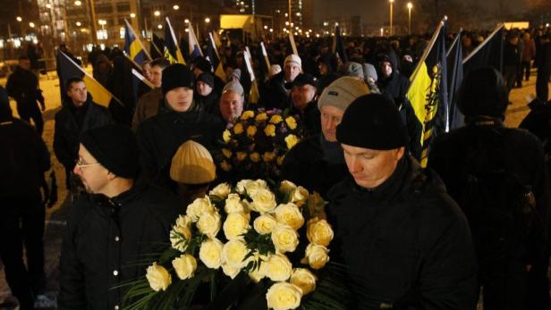 Eine Menschenmenge mit ukrainischen Flaggen und Blumen bei einer Gedenkveranstaltung.