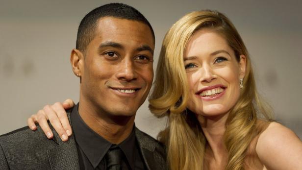 Ein Mann und eine Frau lächeln auf einem roten Teppich in die Kamera.