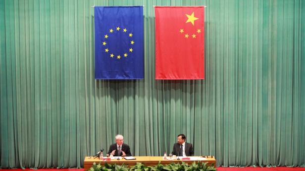 Zwei Männer sitzen an einem Tisch unter den Flaggen der EU und Chinas.