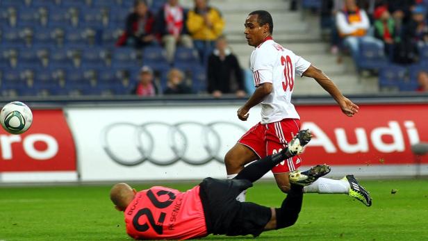 Ein Fußballspieler schießt den Ball, während der Torwart zu Boden geht.